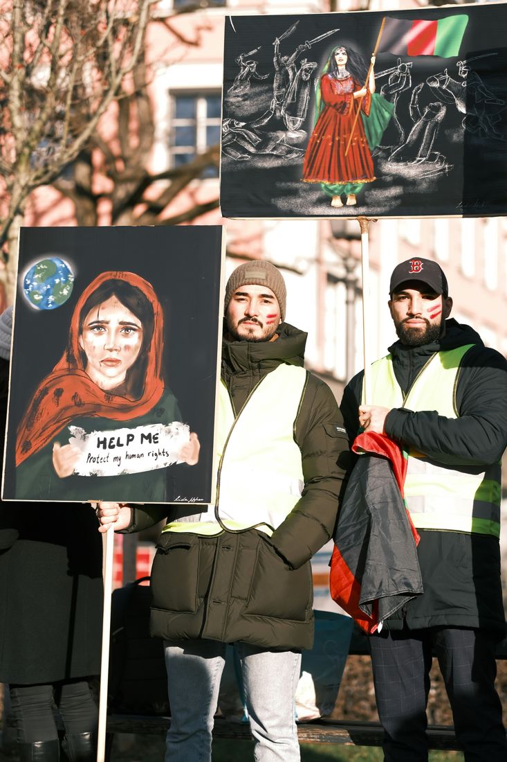 Deux manifestants et une affiche représentant une femme afghane : « Help me, protect my human rights »